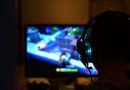 chłopak grający w grę komputerową, odwrócony i w słuchawkach, patrzy na jasny ekran