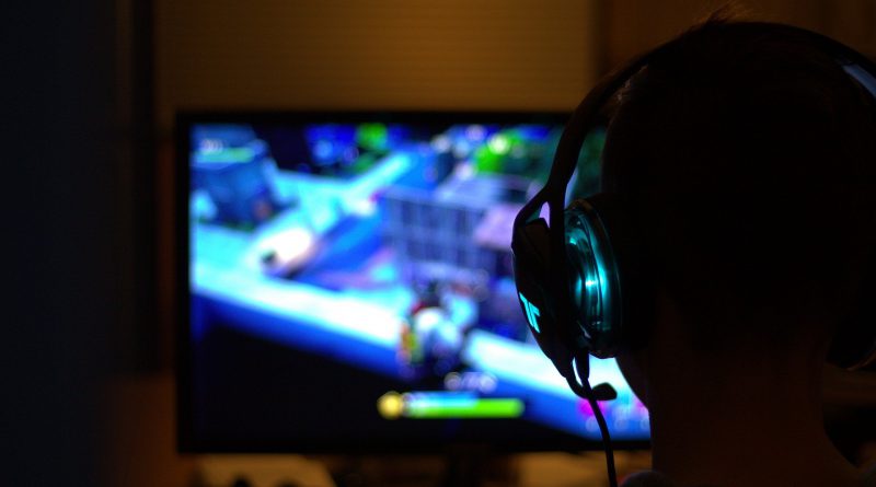 chłopak grający w grę komputerową, odwrócony i w słuchawkach, patrzy na jasny ekran