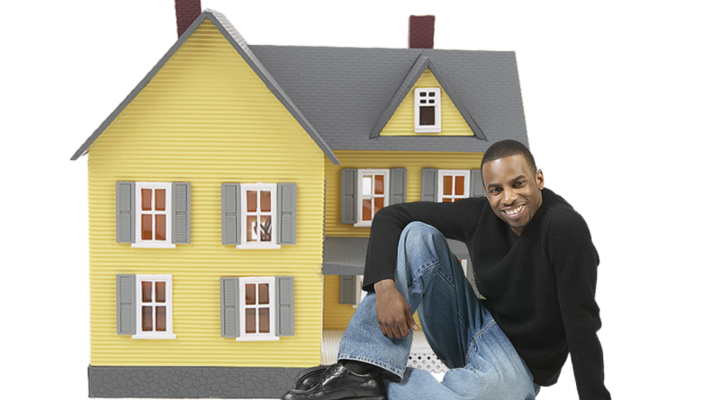czarnoskóry mężczyzna siedzi przed zabawkowym domem, uśmiecha się